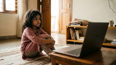 A quiet child watching a coach on a laptop from the edge of a mat